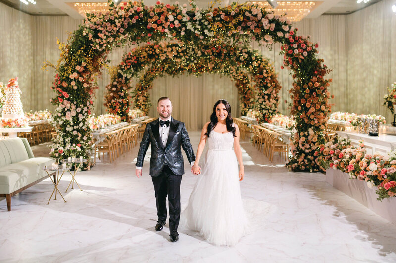 Bride and groom walking beneath an elaborate floral archway